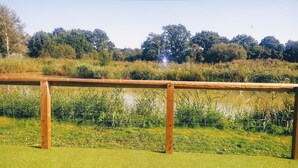 A wooden fence with a grassy field and a body of water in the background. - Lillibelles lake house (Ashford)