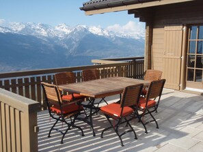 Une terrasse en bois avec une table et des chaises, offrant une vue sur des montagnes enneigées.
