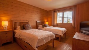 Quarto de cabana de madeira com duas camas, uma televisão e uma janela com vista para as montanhas.