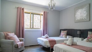 A bedroom with two beds, a chair, a nightstand, a chandelier, and a window with curtains. - Casa Alma 
Beautiful Villa with Mountain & Sea Views
3 Bedrooms 2 Bathrooms (Chayofa)