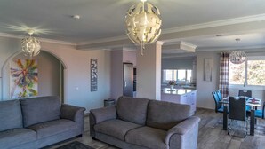 A modern living room with a grey sofa, a dining area with a table and chairs, and a kitchen in the background. - Casa Alma 
Beautiful Villa with Mountain & Sea Views
3 Bedrooms 2 Bathrooms (Chayofa)