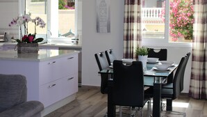 A modern kitchen with white cabinets, a dining area with a glass table, black chairs, and a view of pink flowers through the window. - Casa Alma 
Beautiful Villa with Mountain & Sea Views
3 Bedrooms 2 Bathrooms (Chayofa)