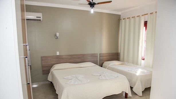 Habitación de hotel con dos camas, ventilador de techo, aire acondicionado y una ventana con cortinas.