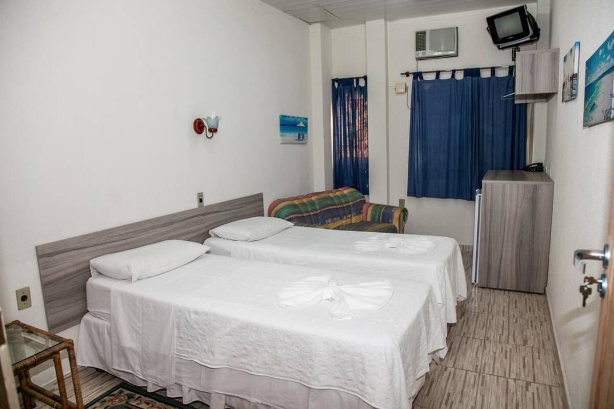 A hotel room with two beds, a TV, a desk, and a window with curtains.