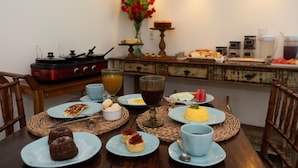 A breakfast setting with plates of food, a coffee machine, and a vase with flowers. - Pousada da Villa (Fernando de Noronha)