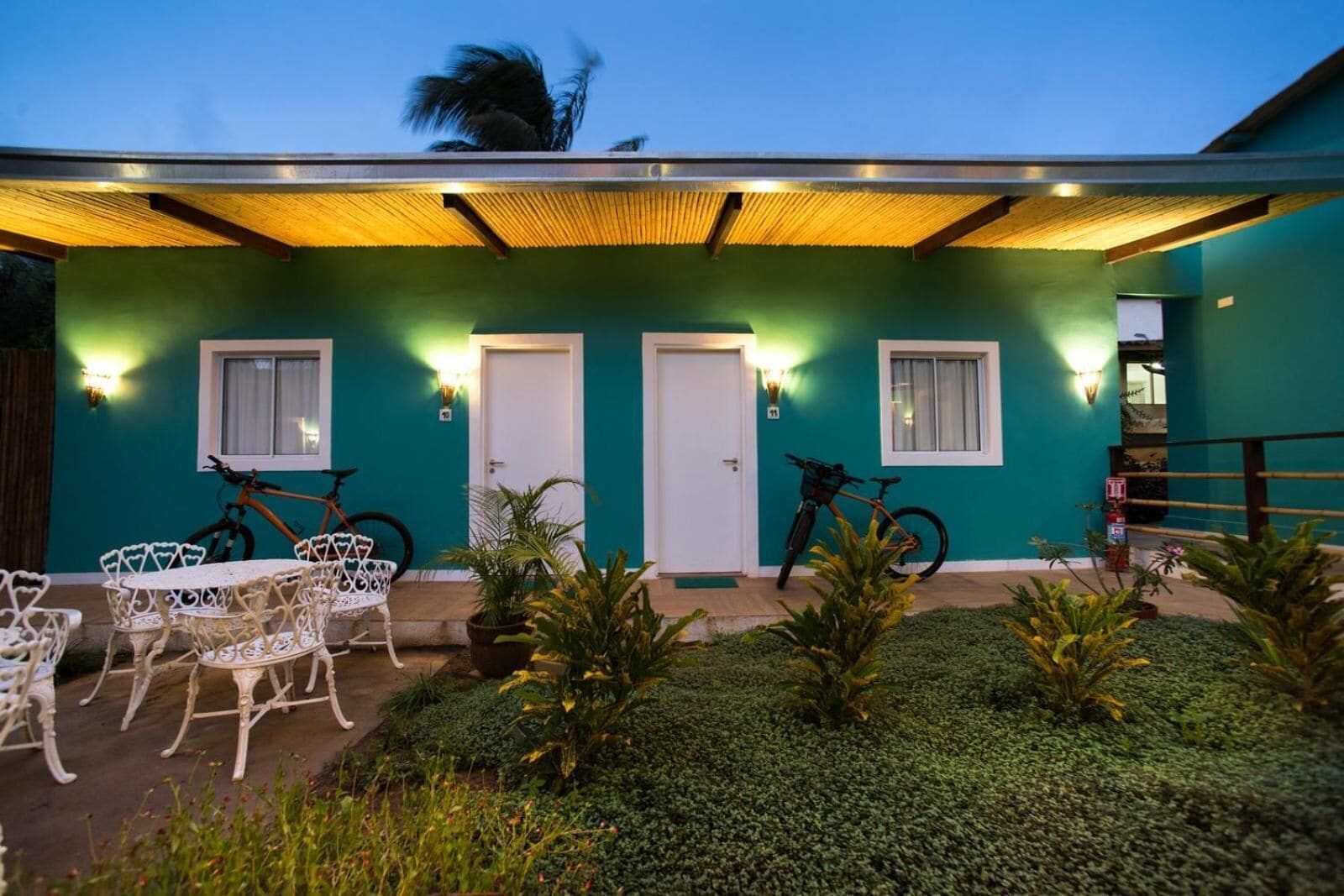 A building with teal walls, two doors, and a covered patio area with white outdoor furniture and bicycles.