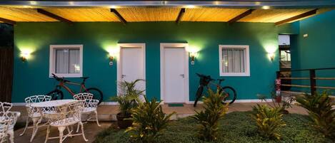 A building with teal walls, two doors, and a covered patio area with white outdoor furniture and bicycles.