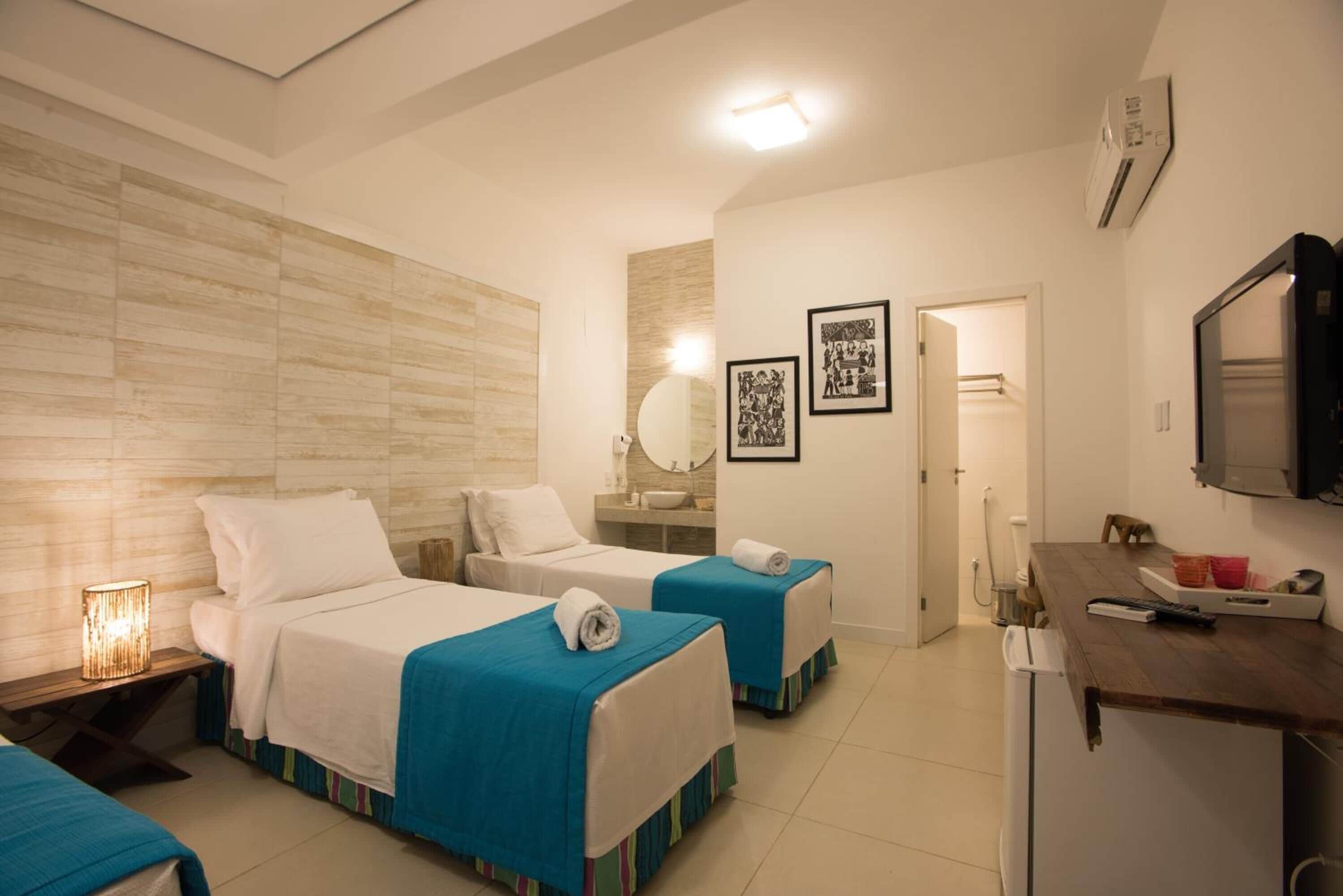 A hotel room with two beds, a small kitchenette, a mirror, and a television.