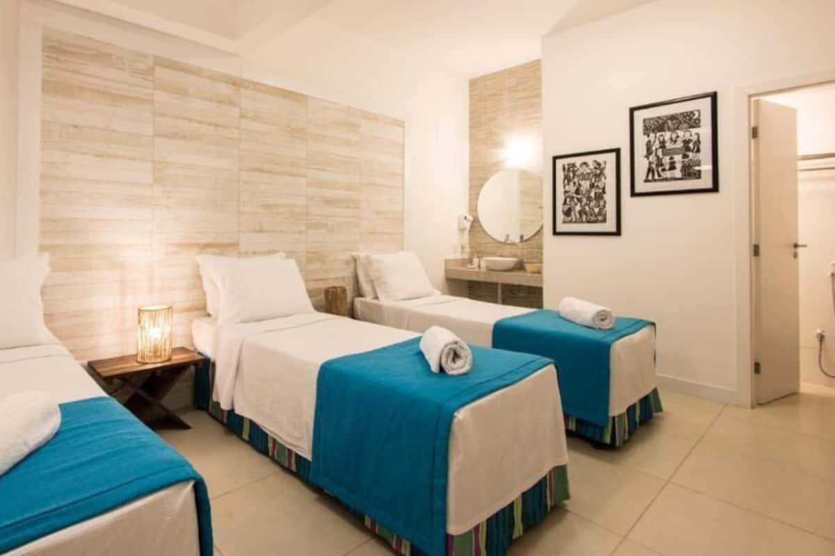 A hotel room with two single beds, a small bedside table with a lamp, a mirror, and framed pictures on the wall.