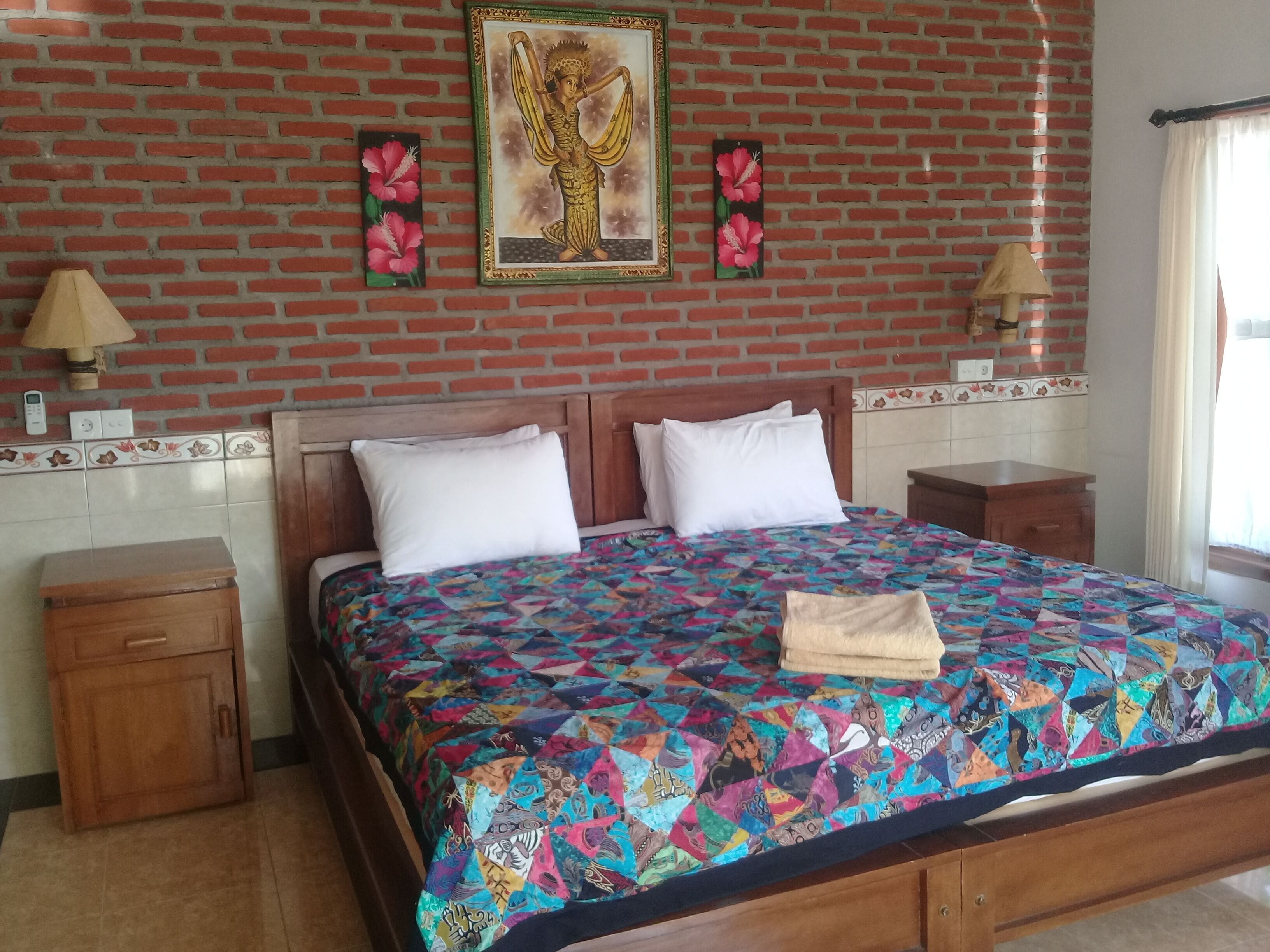 Ein Schlafzimmer mit einer Ziegelwand, einem Bett mit farbenfroher Steppdecke, zwei Nachttischen und einem Beistelltisch.