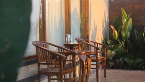 A wooden table and chairs set up on a tiled patio with a view of a brick wall and green plants.