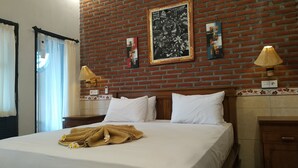 A hotel room with a brick wall, a bed with white linens, two bedside lamps, and a large framed artwork above the bed.