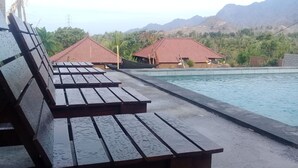 A poolside area with wooden benches, a swimming pool, and buildings with red roofs in the background.