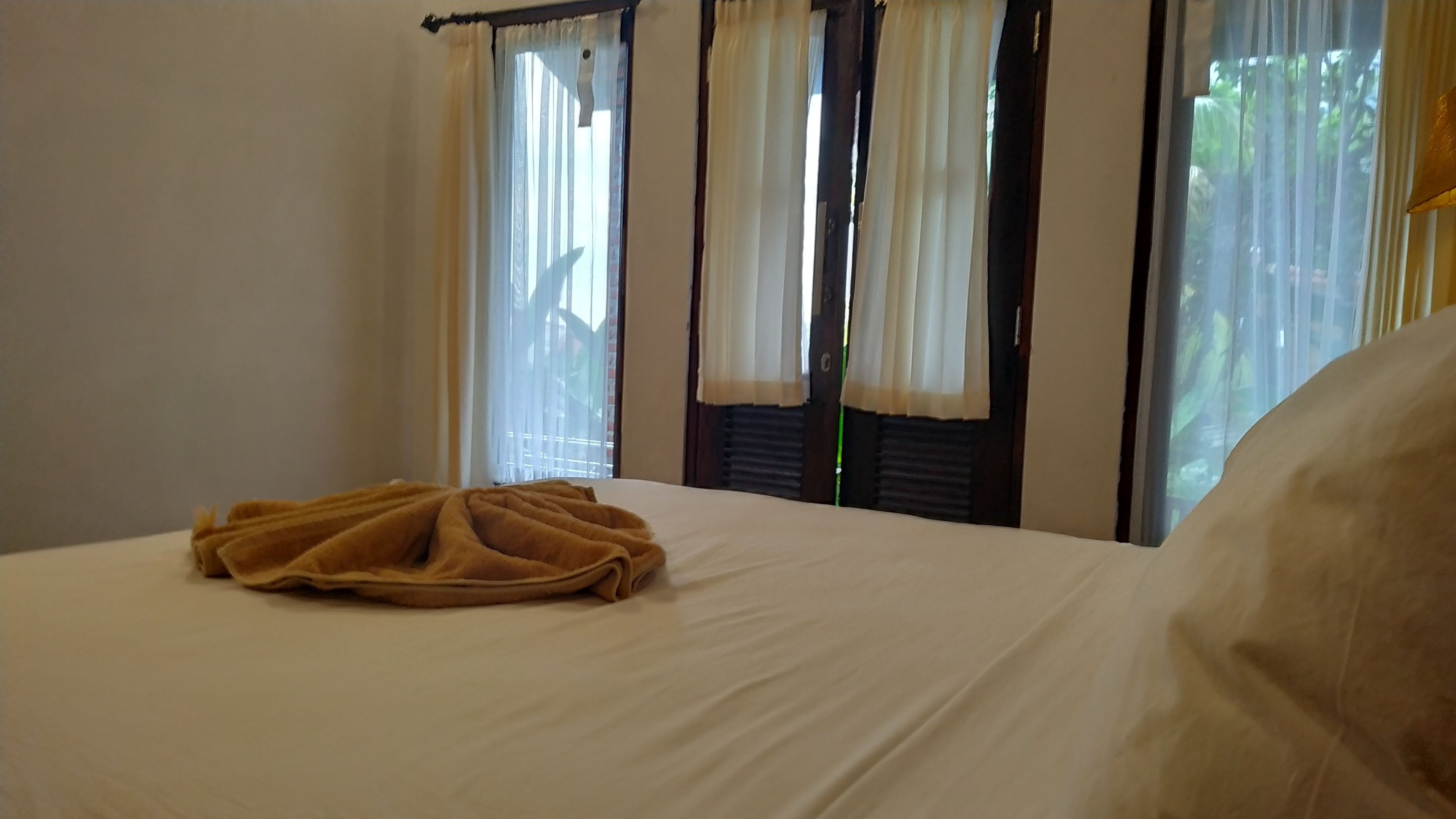 Habitación de hotel con una cama, una ventana con cortinas y vistas a zonas verdes.