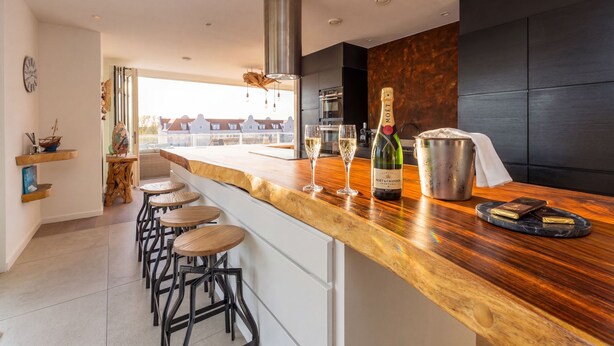 Une cuisine moderne avec un plan de travail en bois, des tabourets de bar et une vue sur les immeubles.