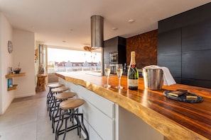 A modern kitchen with a wooden countertop, bar stools, and a view of buildings.