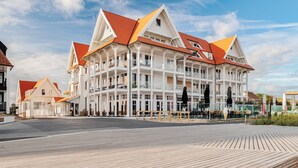 Un hotel a più piani con tetto rosso e facciata bianca, con balconi e una zona terrazza in legno.