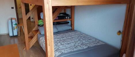 A bunk bed room with a desk and chair, a small table, and a door.