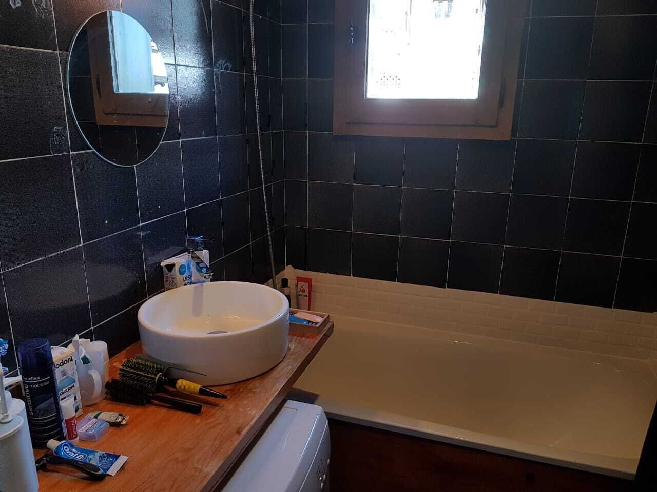 A bathroom with a bathtub, a round sink, and a mirror.