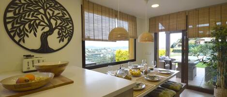 A modern kitchen with a large island, a dining area with a view, and a decorative tree wall art piece.
