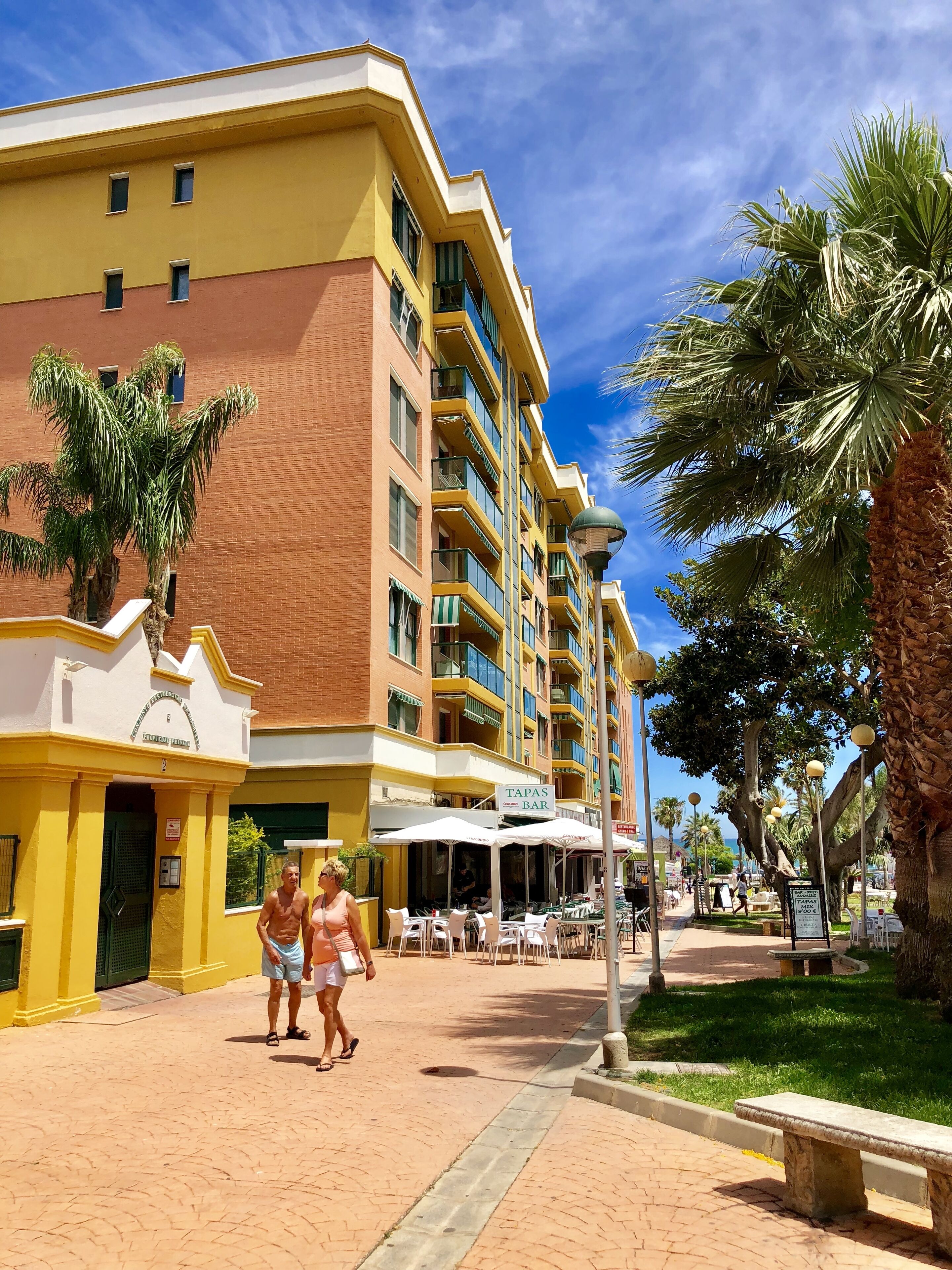 A hotel with a yellow facade, multiple balconies, and outdoor seating areas.