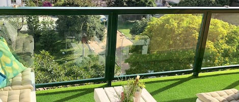 Un balcón con césped artificial, un banco blanco y una planta en maceta.
