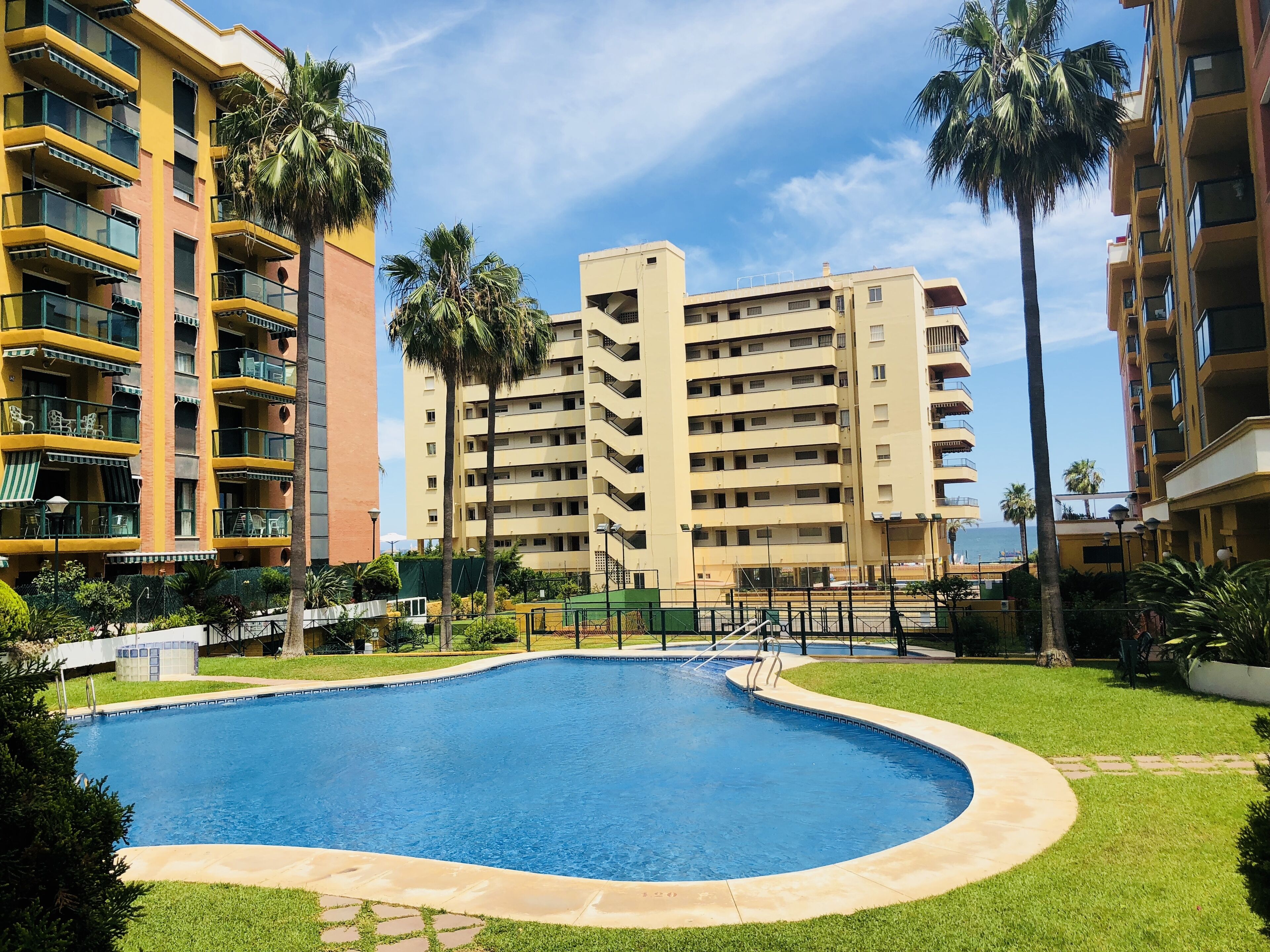 A swimming pool surrounded by a well-maintained lawn, with tall buildings in the background.