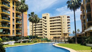 A swimming pool surrounded by a well-maintained lawn, with tall buildings in the background. - Luxury apartment Bajondillo on the beach (TORREMOLINOS)