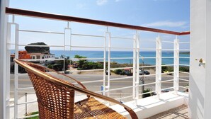 A balcony with a wicker chair, white railings, and a view of the ocean and a street with buildings and cars. - Hang Hai B & B (Hengchun)
