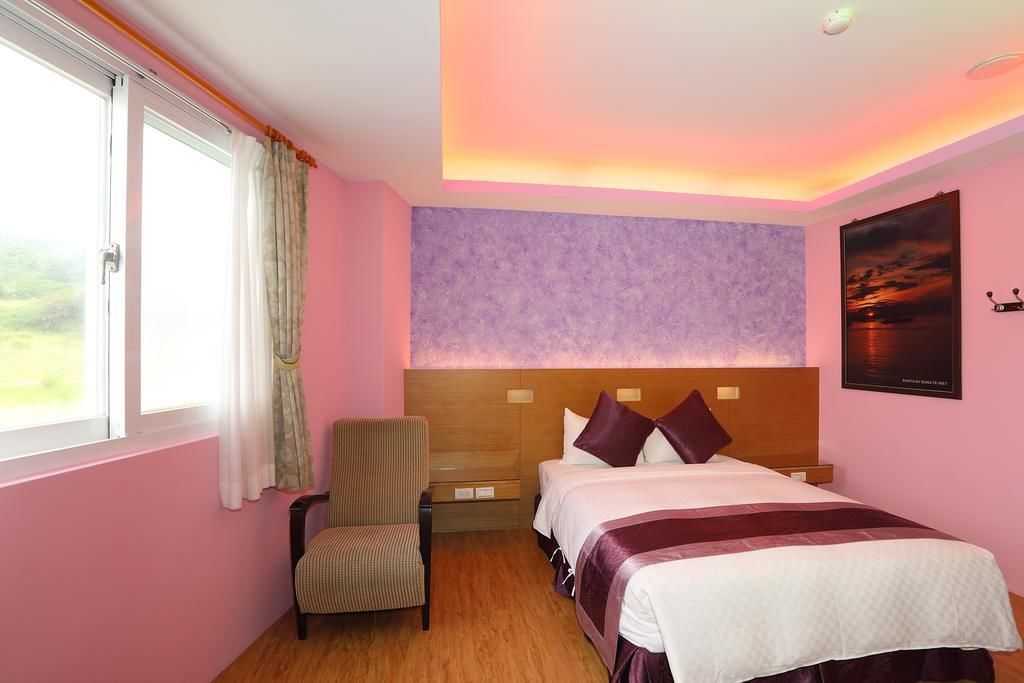 A hotel room with a bed, a chair, a nightstand, and a window with curtains.
