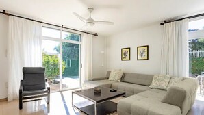 A modern living room with a sofa, a coffee table, and a chair. There are two framed pictures on the wall and a ceiling fan.