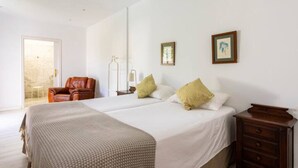 A hotel room with two beds, a leather armchair, a nightstand, and a door leading to a balcony.