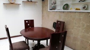 A dining area with a round wooden table and four chairs, a white shelf with decorative plates, and a stone wall. - Apartamento Amoblado El Dorado (Bogotá)
