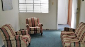 A room with three striped armchairs and a sofa, a blue carpet, and a window with blinds. - Apartamento Amoblado El Dorado (Bogotá)