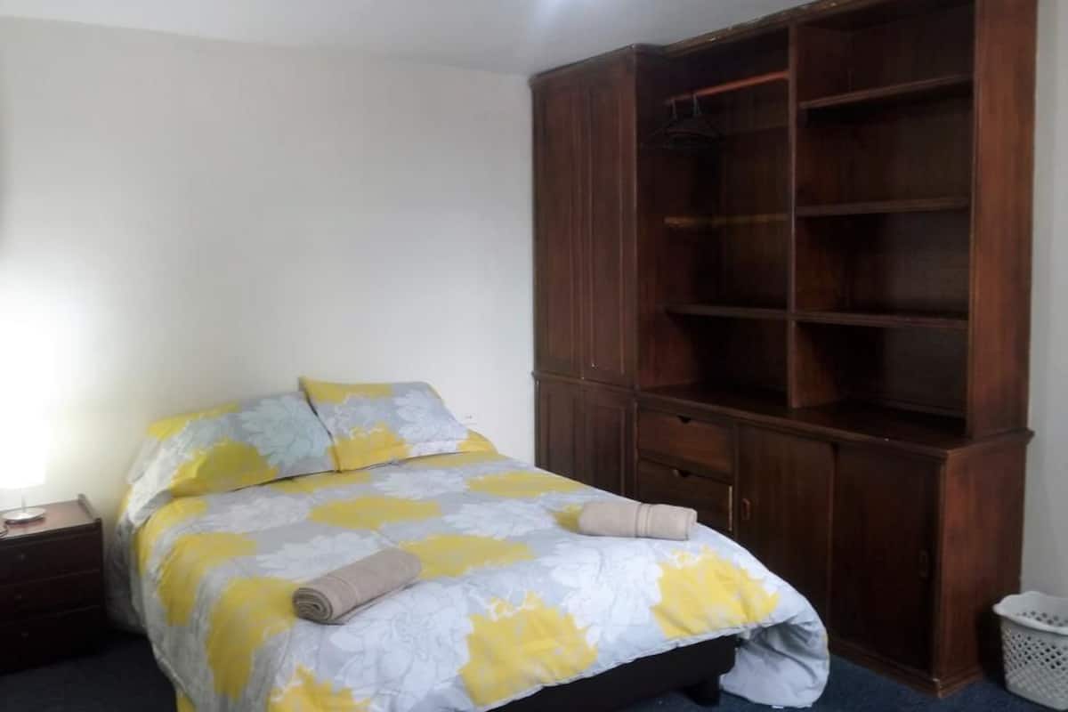 A bedroom with a bed, a wooden wardrobe, a nightstand, and a laundry basket.