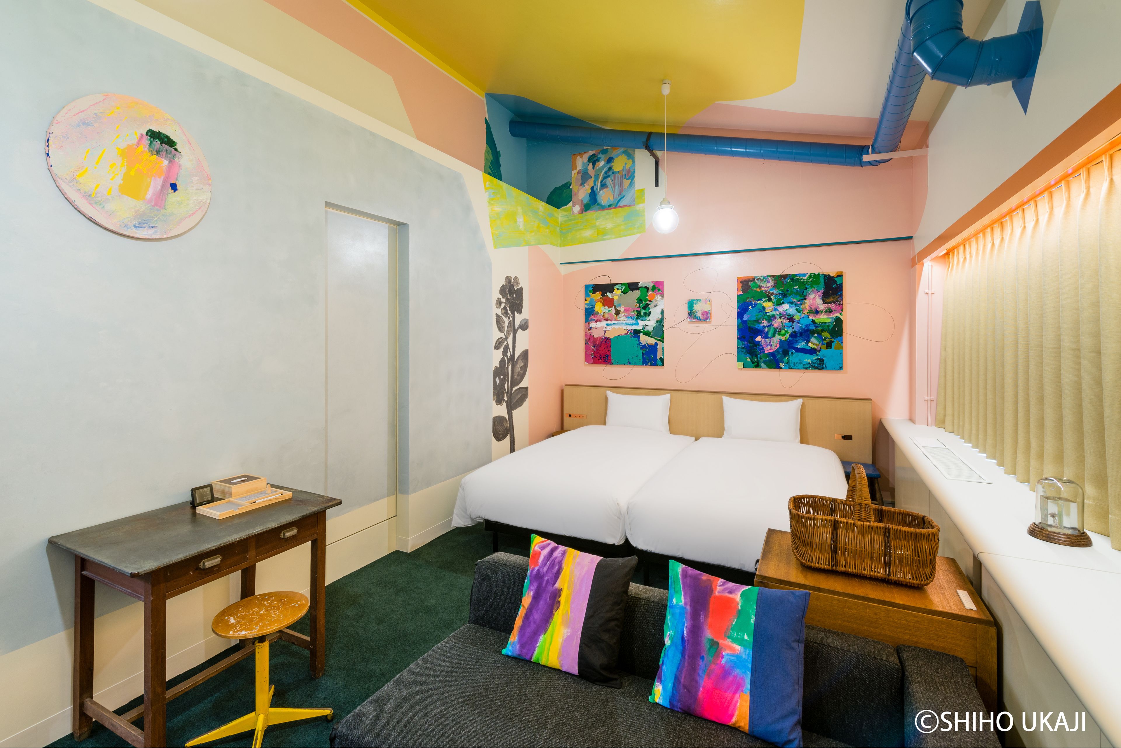 A hotel room with a bed, a desk, a chair, and a window with blinds.