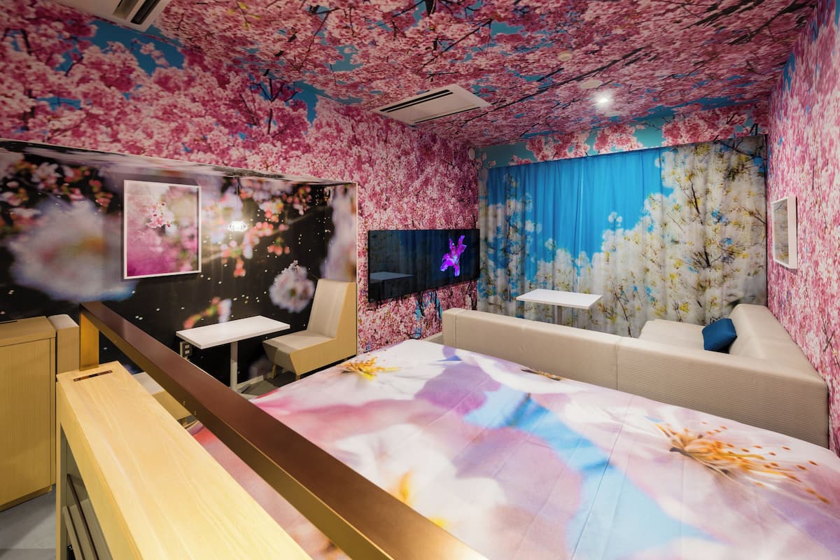 Una habitación con papel tapiz de flores de cerezo, un televisor de pantalla plana, un sofá y un escritorio.