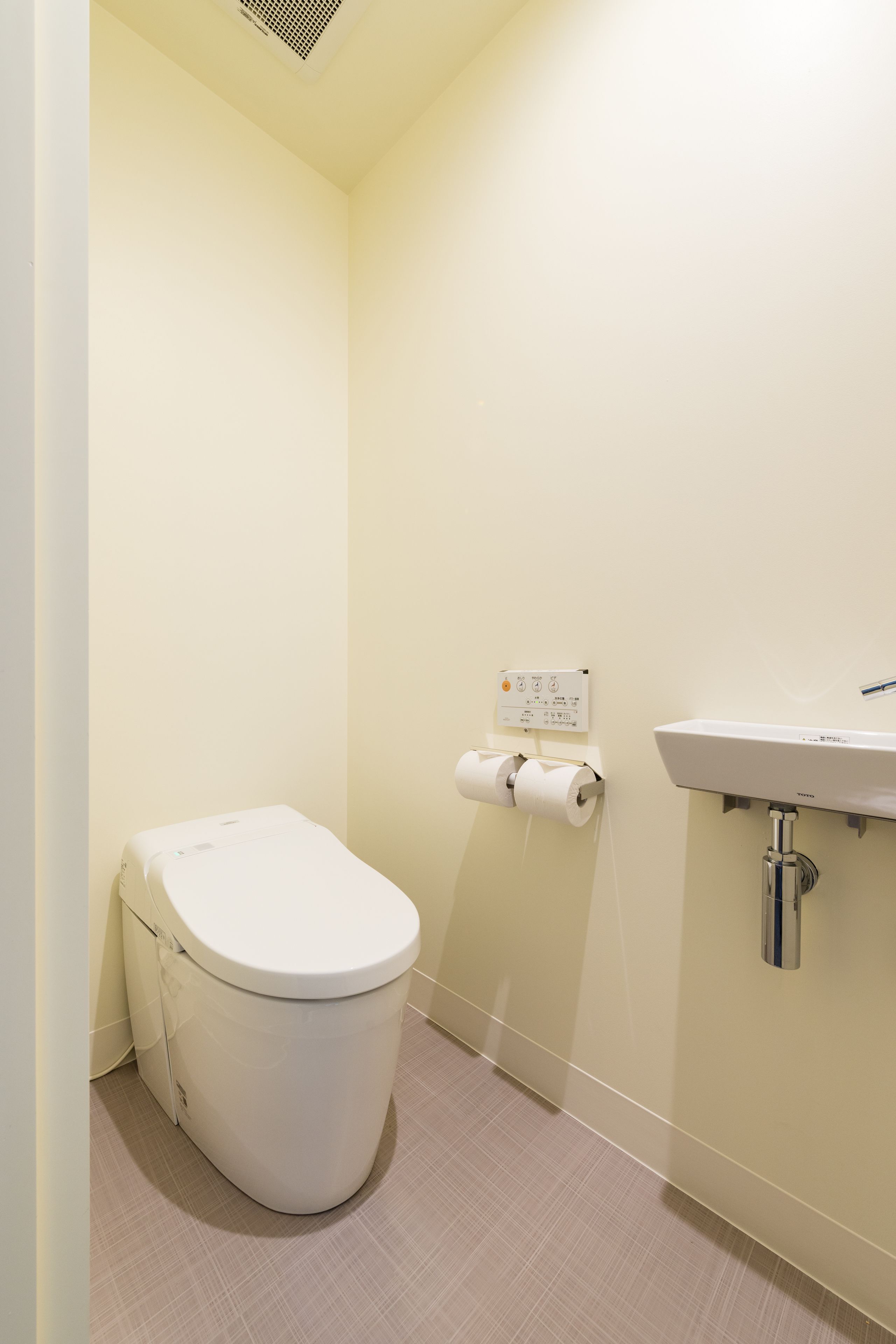 A small, clean bathroom with a toilet, a wall-mounted sink, and a toilet paper holder.