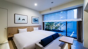 Een moderne hotelkamer met een groot bed, een kleine tafel en uitzicht op groen door een groot raam.