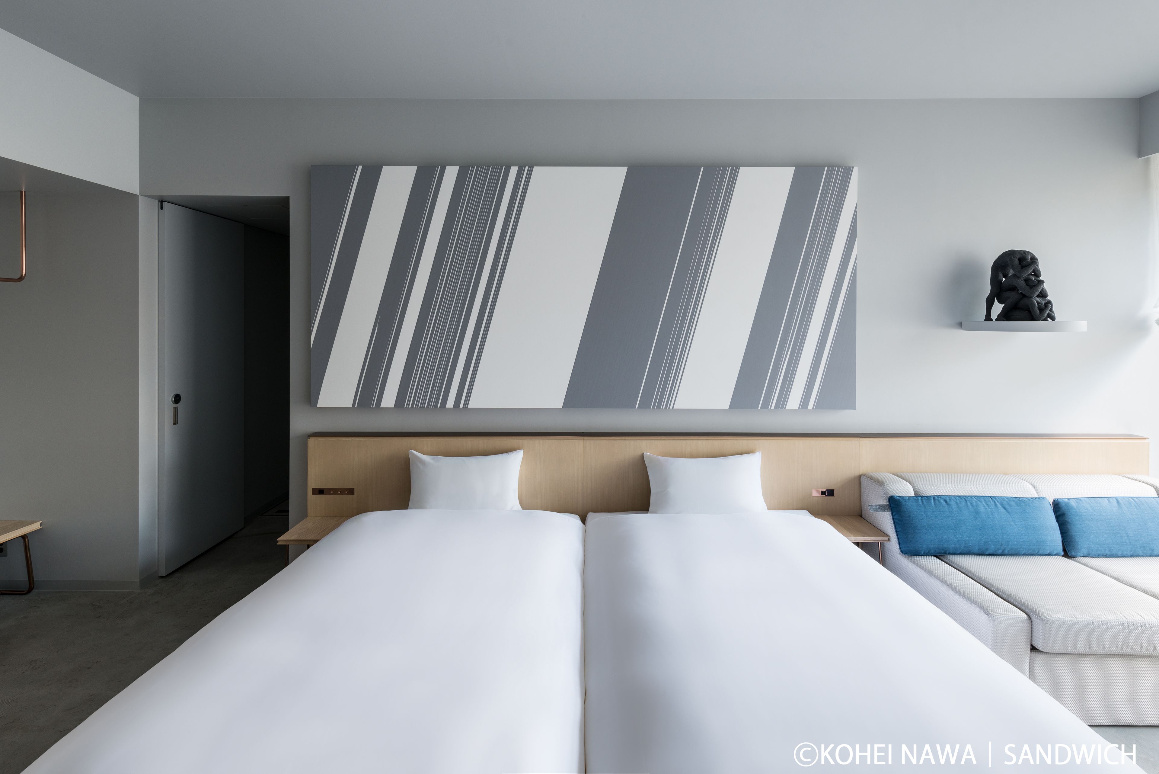 A modern hotel room with a large bed, a sofa, and a wall-mounted artwork.