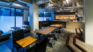 Een moderne bar met houten tafels en stoelen, een bargedeelte met flessen en grote ramen met uitzicht op een straat met bomen.