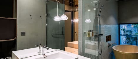 A modern bathroom with a large mirror, two sinks, a freestanding bathtub, and a glass-enclosed shower area.