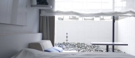 Habitación de hotel moderna con cama, una mesita y vistas a un paisaje urbano a través de amplios ventanales.