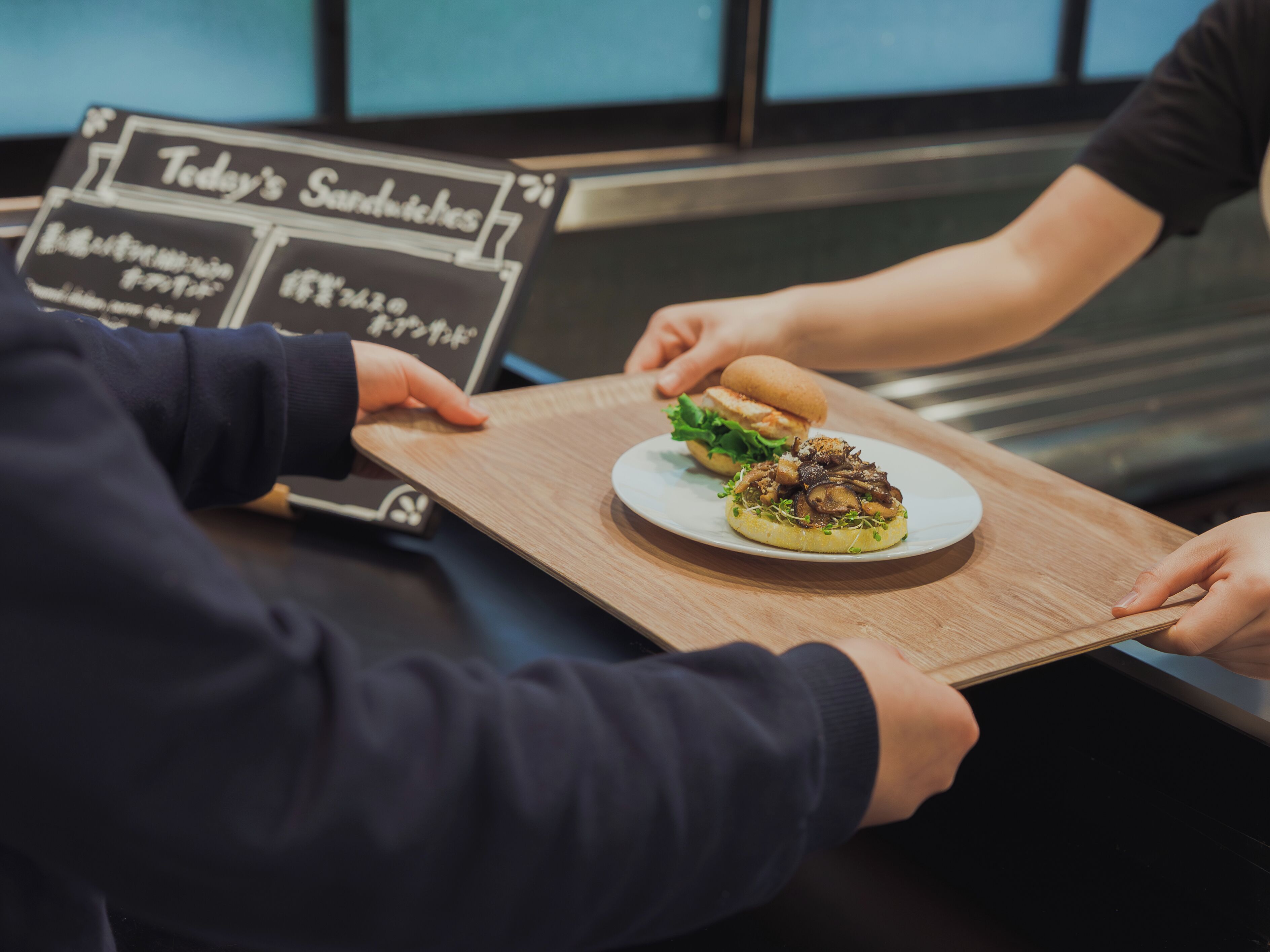 Una persona sostiene una bandeja con un sándwich y un plato pequeño con ensalada.