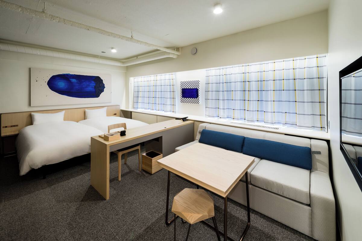Habitación de hotel con cama, escritorio, zona de estar y un gran ventanal con cortinas.