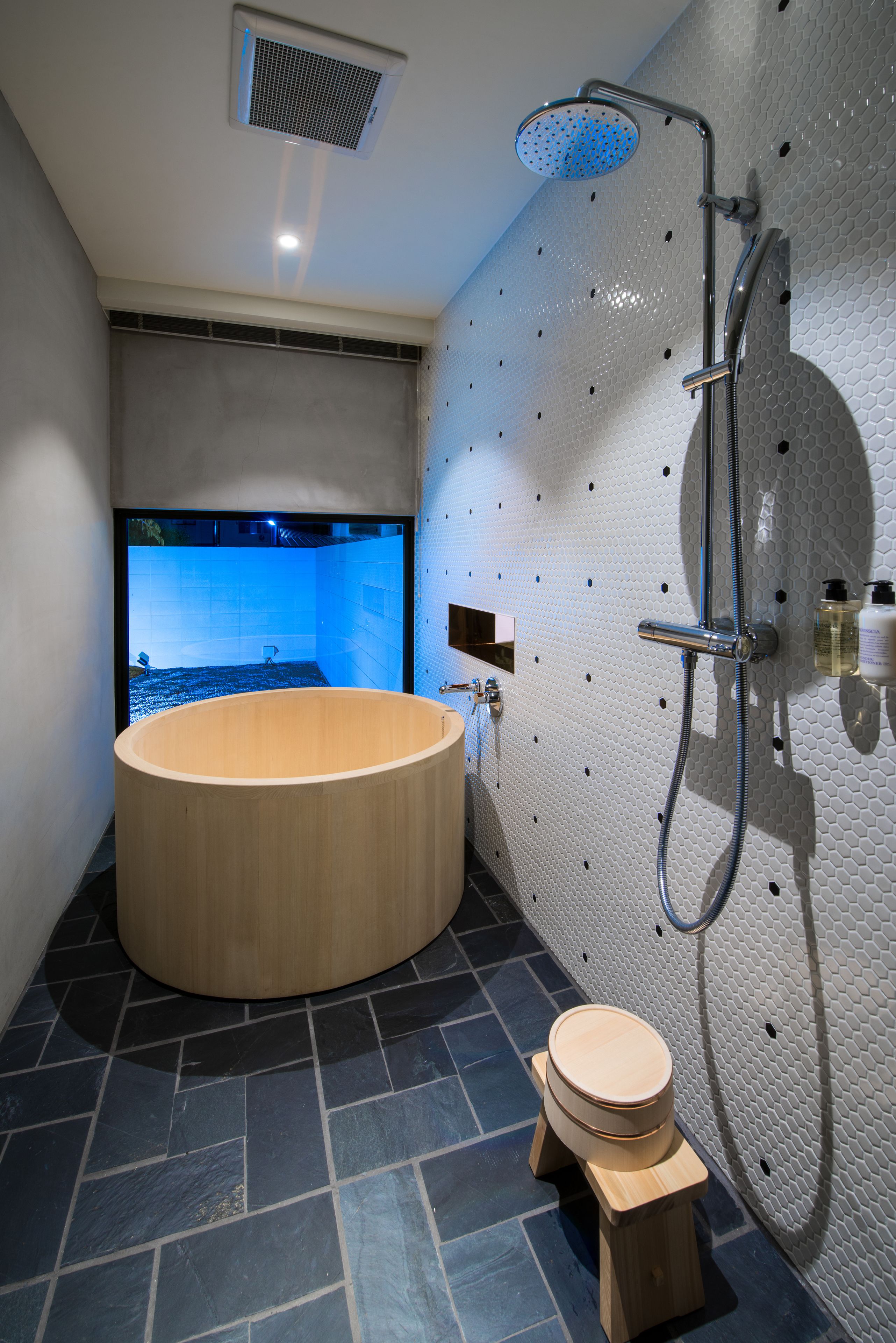 A modern bathroom with a large wooden bathtub, a shower, and a small wooden stool.