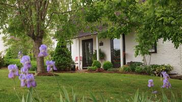 A white house with a dark door, surrounded by a well-maintained lawn and purple flowers.
