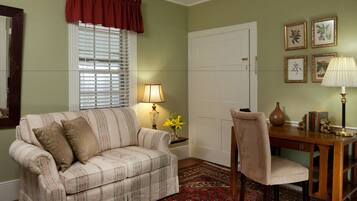 A room with a striped sofa, a wooden desk, a vase with flowers, and framed botanical prints on the wall.