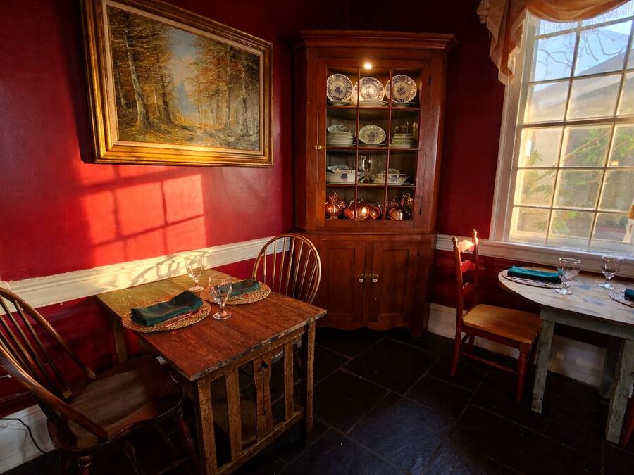 A dining area with a wooden table, chairs, a cabinet with dishes, and a painting on the wall.