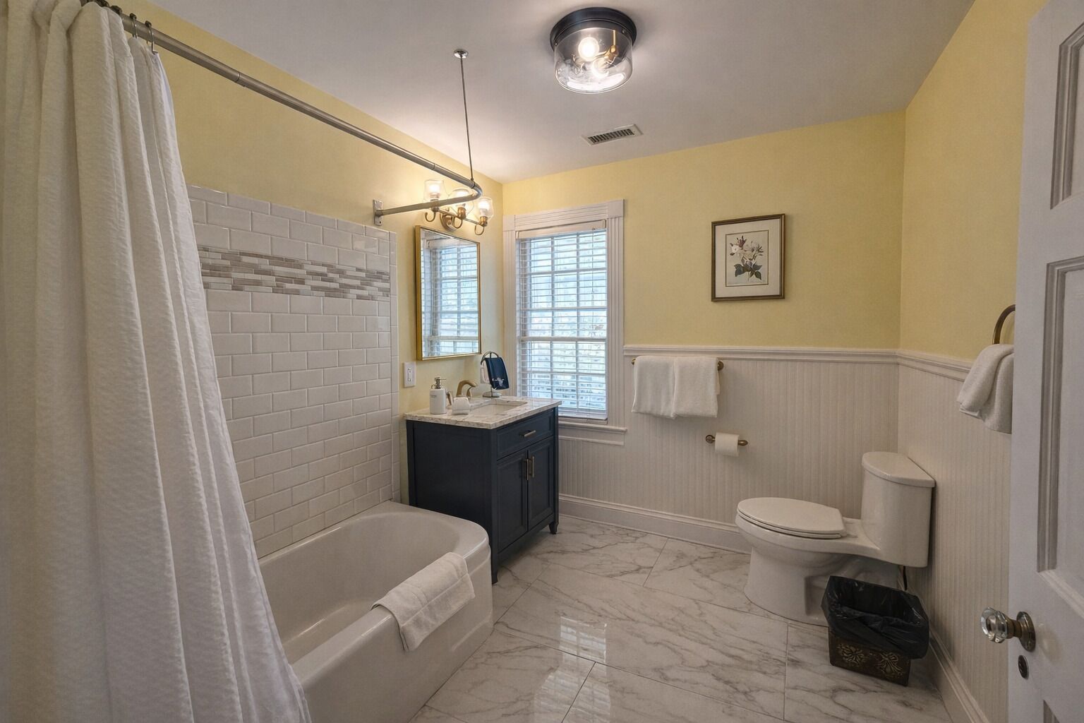 Ein Badezimmer mit Badewanne, Waschbecken, Toilette und einem Fenster mit Jalousien.